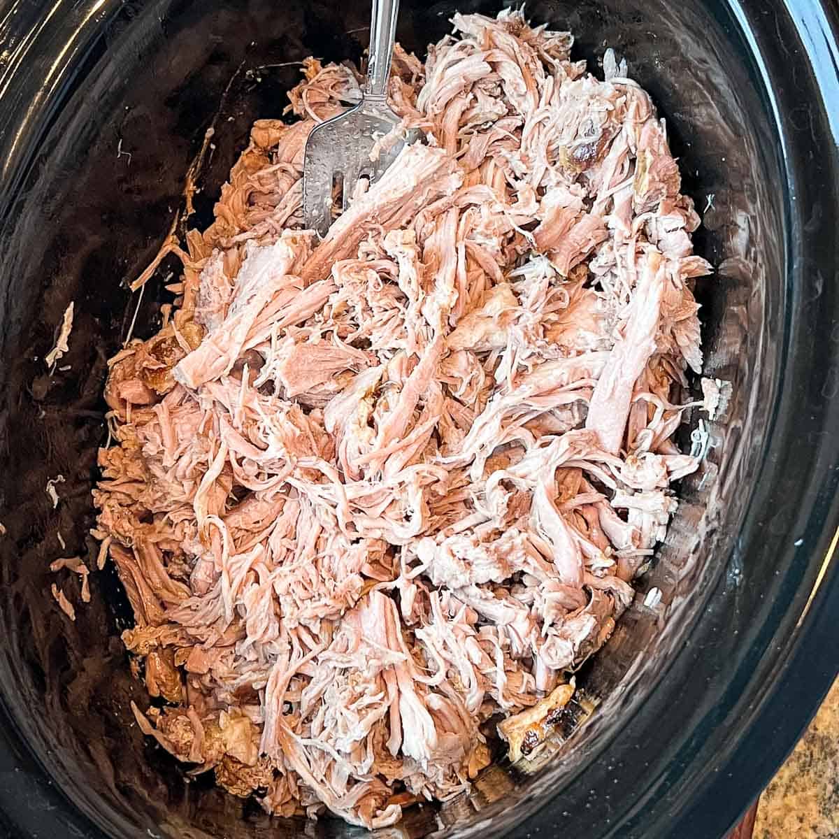 Shredded pulled pork in a crock pot with a fork.