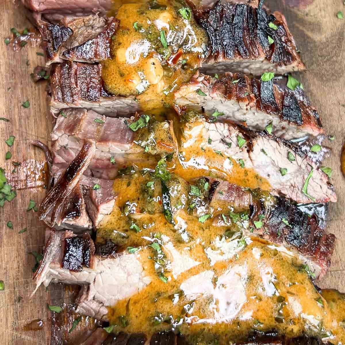 Sliced Grilled Ribeye Steak drizzled with warm Cowboy Butter Sauce and garnished with fresh herbs.