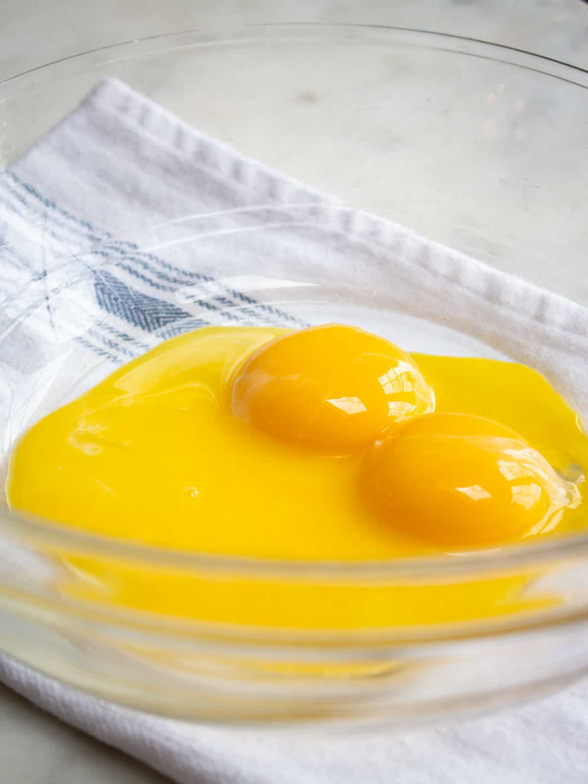 Egg yolks in a clear glass bowl placed on a white and blue striped napkin.