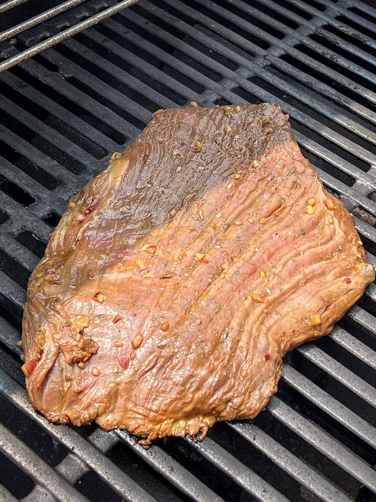 Marinated flank steak on grill grates.