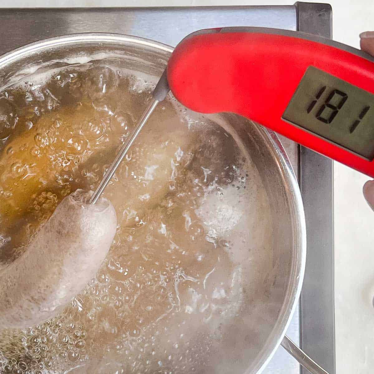 Brats boiling in beer with a red instant-read thermometer inserted into a brat reading 181°F.