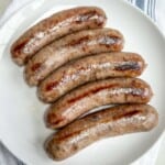 5 grilled beer brats lined up on a white plate.