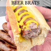 A grilled beer brat with yellow mustard in a bun being held up with a title banner at top of image.