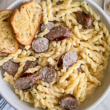 A bowlful of Creamy Bratwurst Pasta with two crostini on the upper left side.