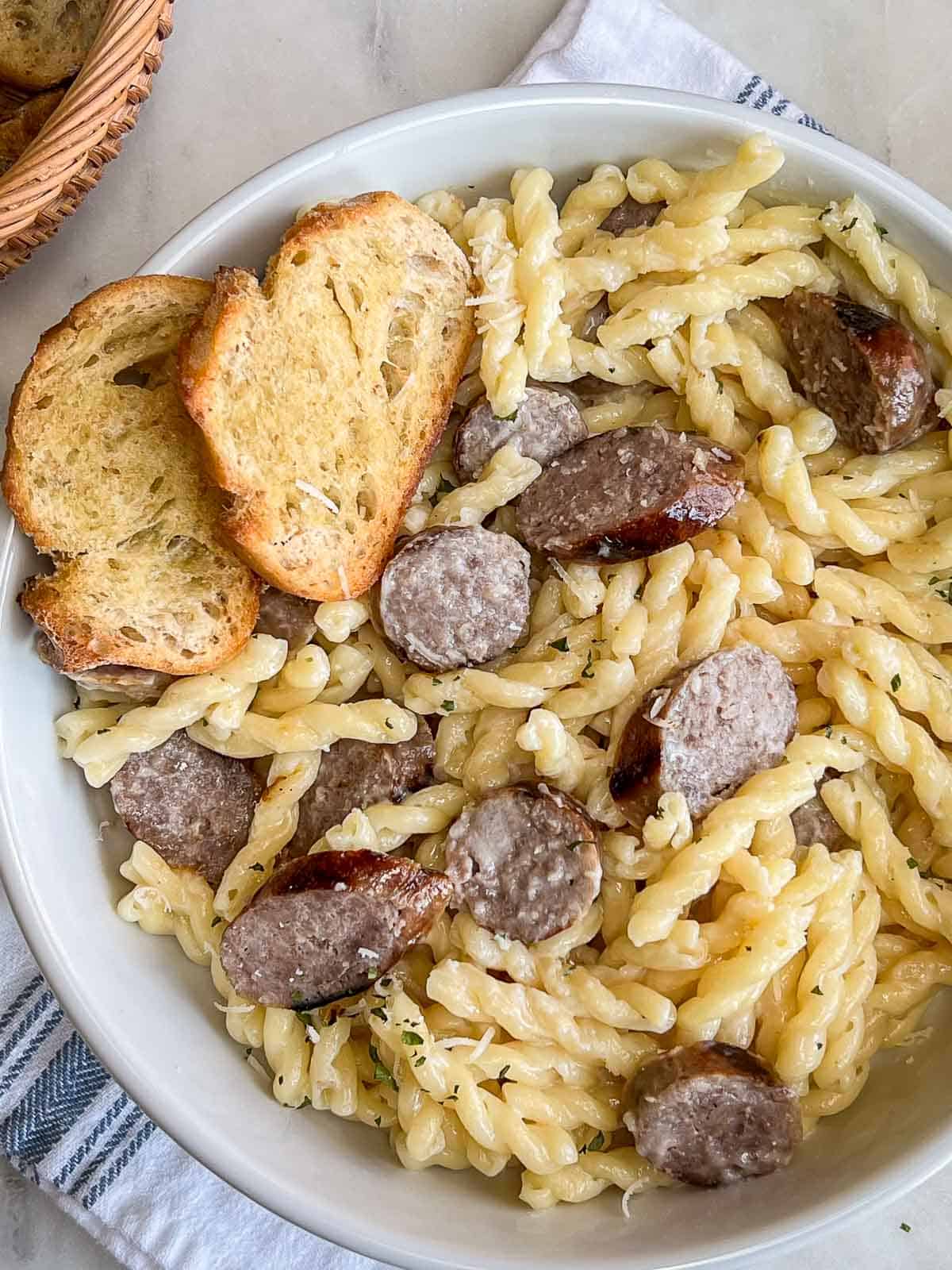 A bowlful of Creamy Bratwurst Pasta with two crostini on the upper left side.