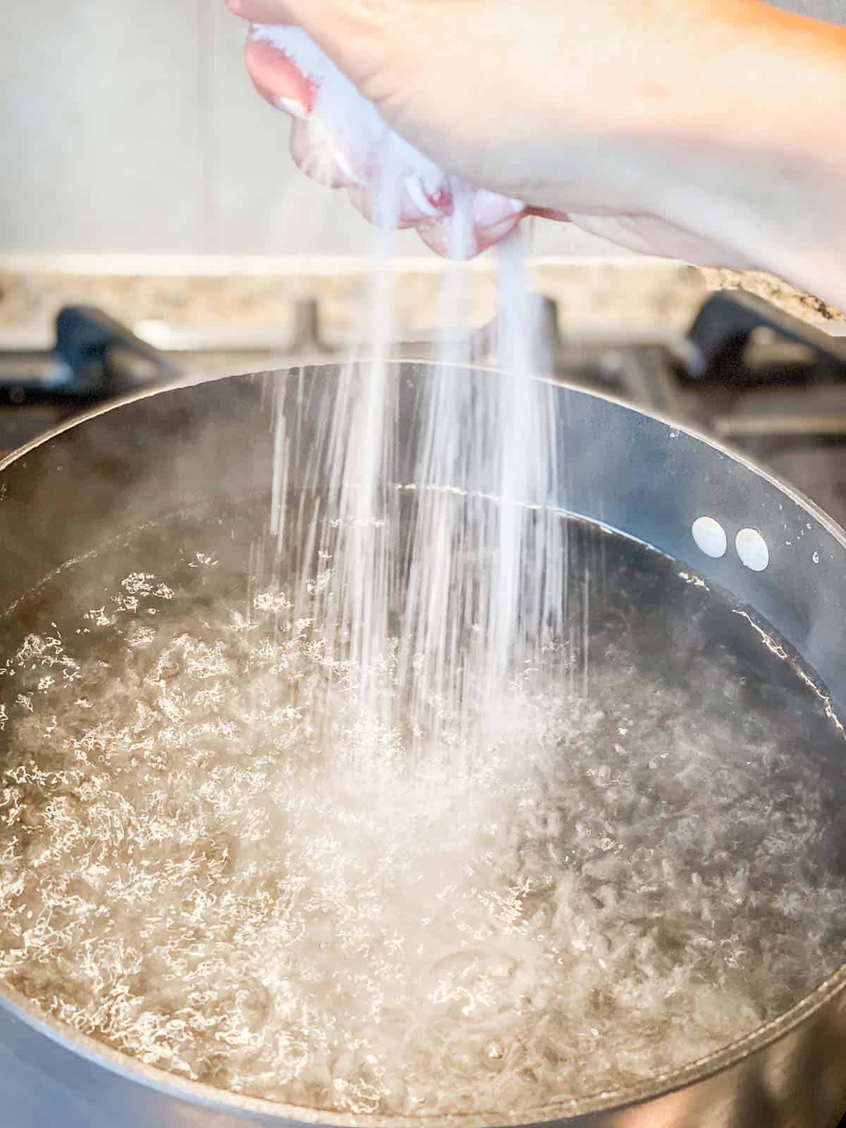 A handful of salt being released into a pot of boiling water.