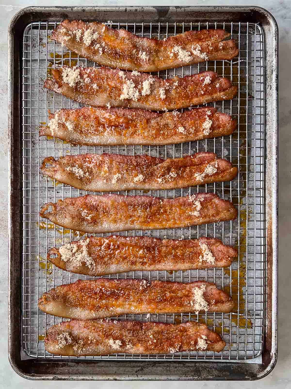 Slices of half cooked candied bacon sprinkled with brown sugar on a backing rack.