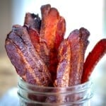 Sweet and spicy candied bacon standing upright in a mason jar.