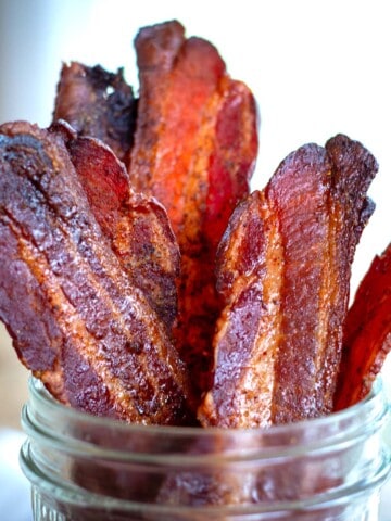 Sweet and spicy candied bacon standing upright in a mason jar.