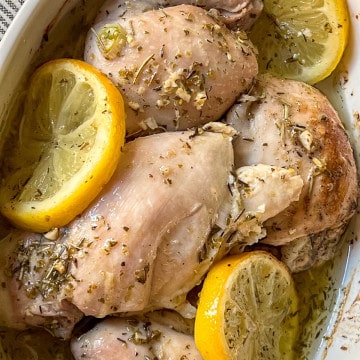 Baked chicken thighs with lemon slices in a white dish.