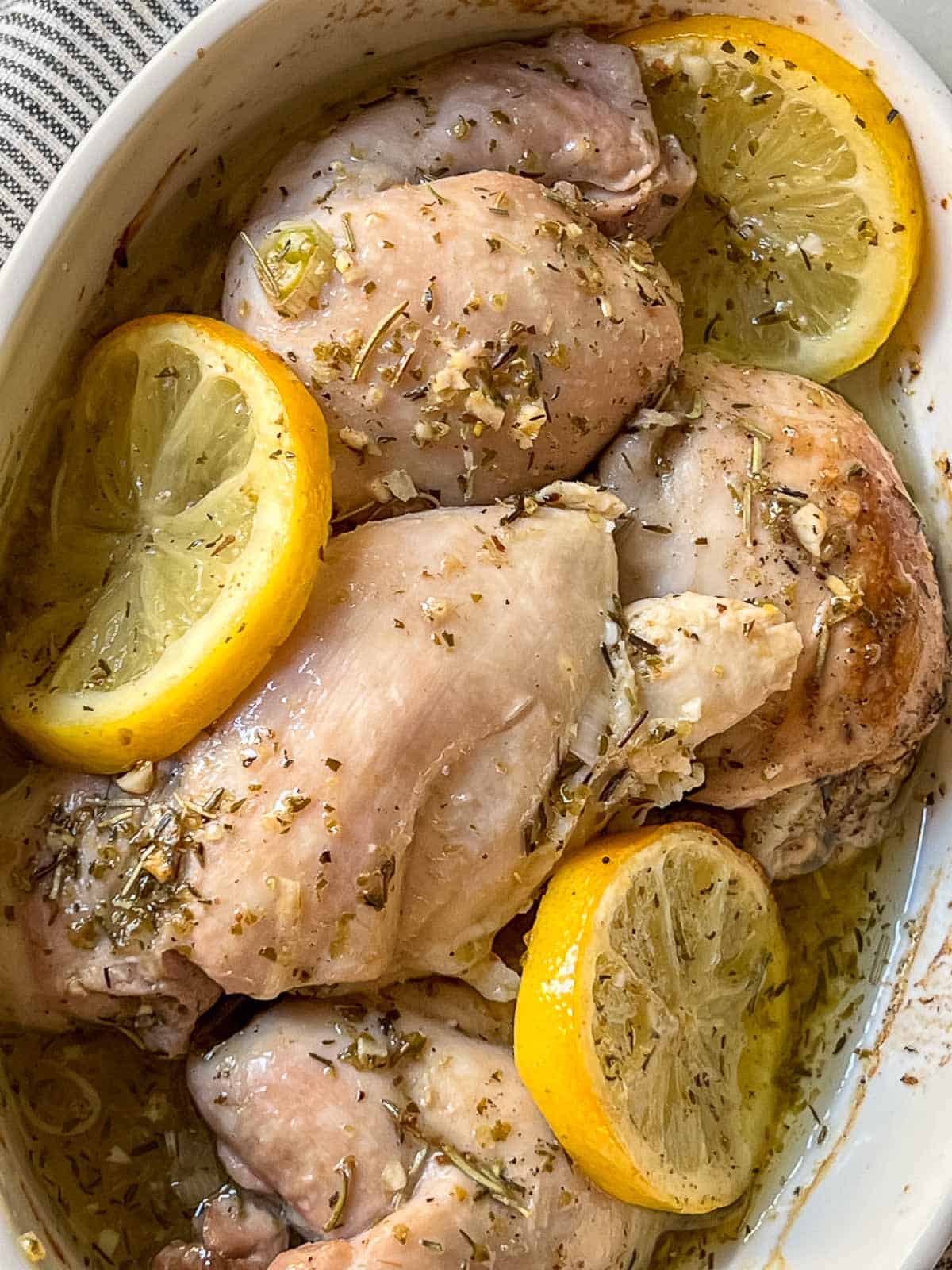 Baked chicken thighs with lemon slices in a white dish.