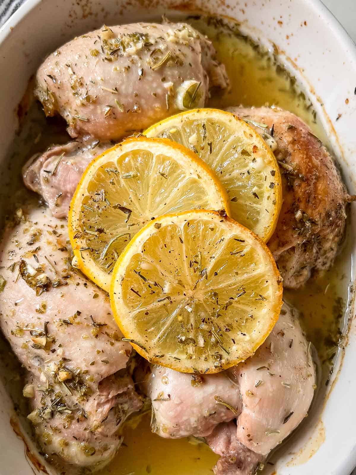 Baked chicken thighs with lemon slices in a white dish.