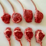 Eight Frenched lamb chops on a white cutting board.
