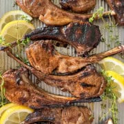 Grilled lamb chops on a tray garnished with lemon and thyme.