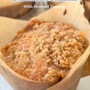 Banana Muffin on a white plate with a muffin tin of same in background.