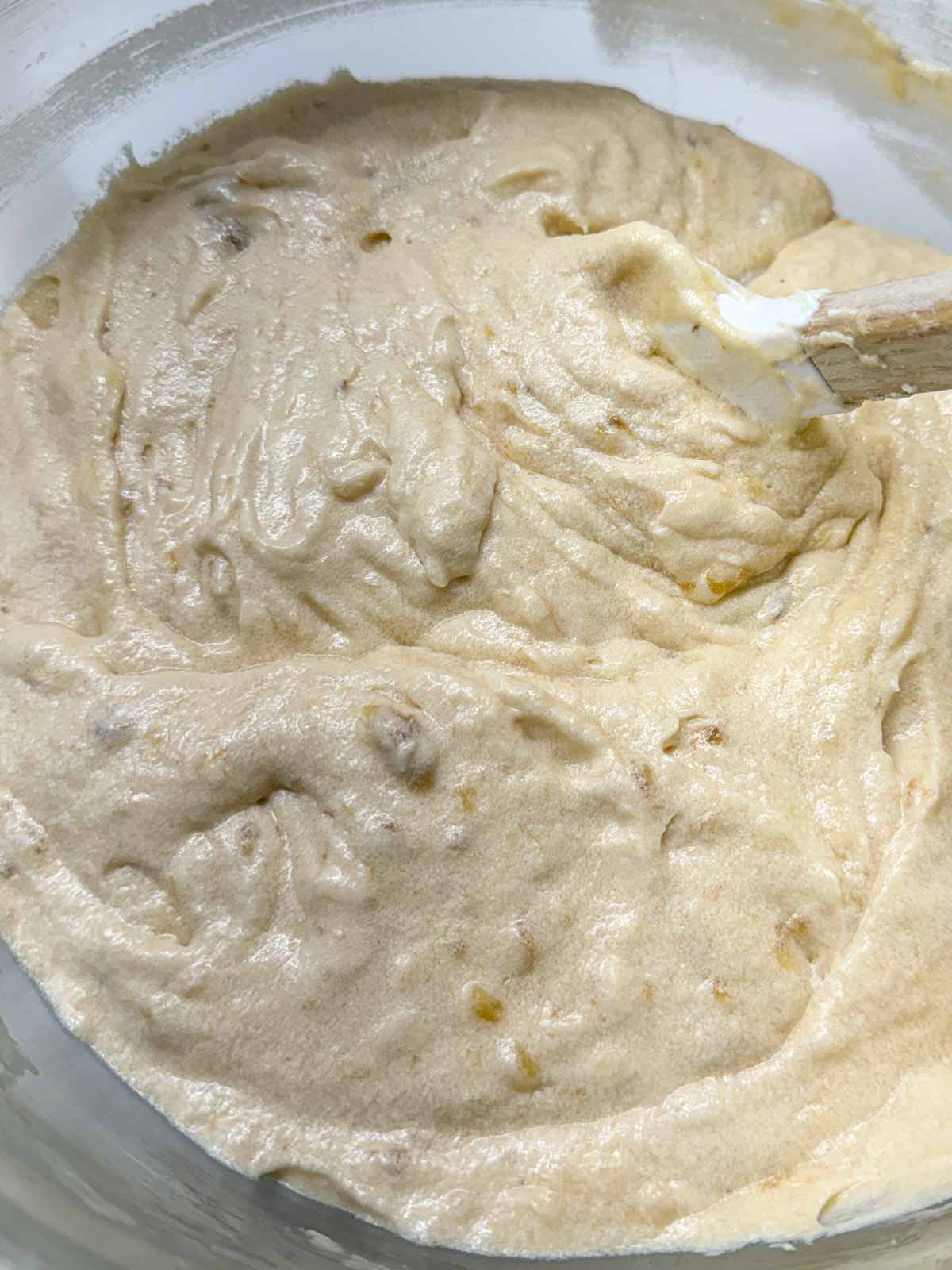Banana muffin batter in a bowl with a rubber spatula to one side.