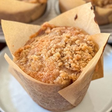 Banana Muffin on a white plate with a muffin tin of same in background.
