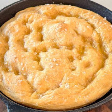 A whole baked focaccia in a cast iron skillet.