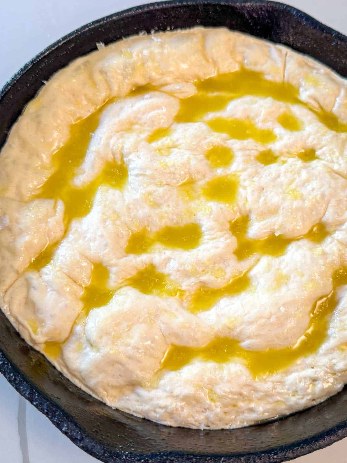 Focaccia dough with olive oil and dimples in a cast iron skillet prepped and ready for the oven.