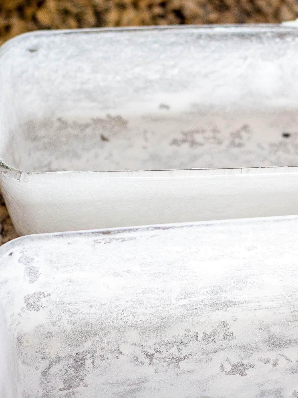 Two buttered and floured loaf pans sitting on a counter.