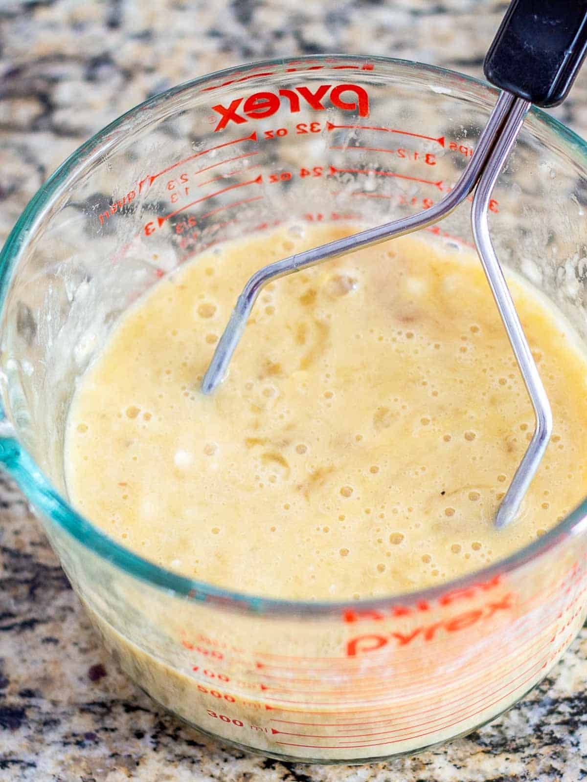 A measuring cup filled with mixed mashed banana, eggs, and vanilla for Banana Bread recipe.