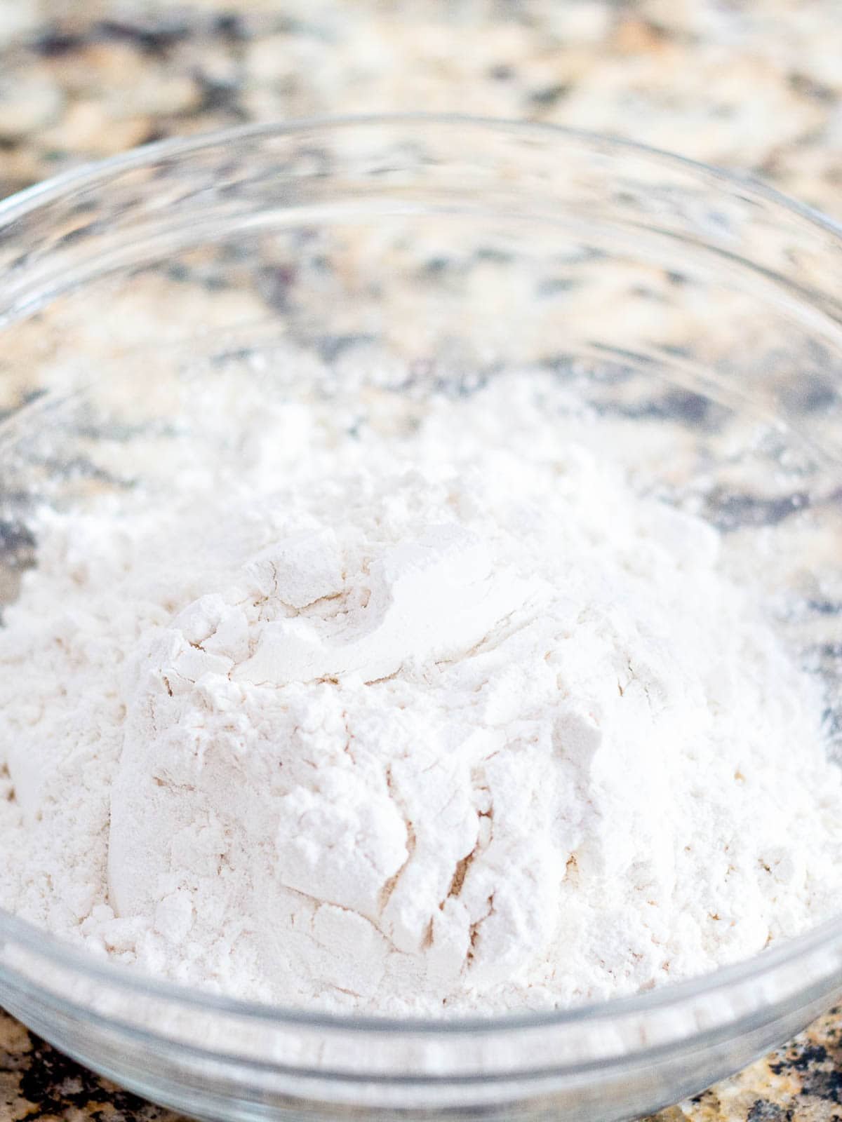 A bowl of flour and other dry ingredients sitting on a counter top.
