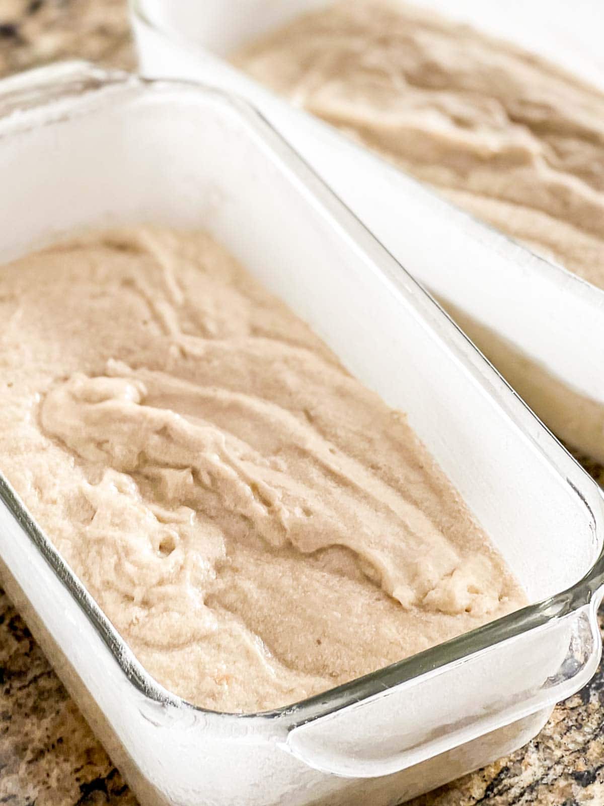 Two loaf pans filled with batter on a counter.