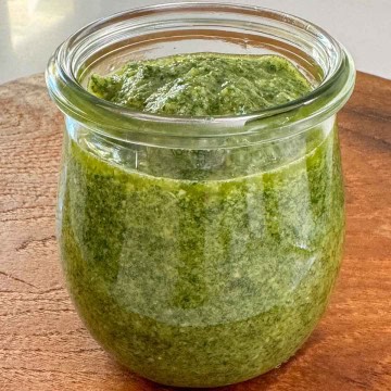 An open jar of homemade basil pesto to show flecked texture.