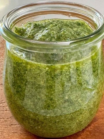 An open jar of homemade basil pesto to show flecked texture.