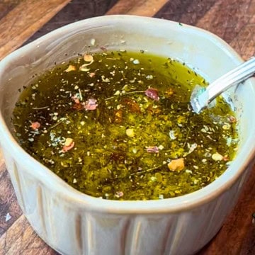 Homemade garlic oil in a small dish with crushed garlic and herbs on a rustic board.