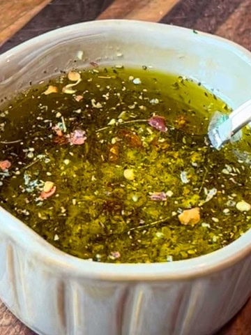 Homemade garlic oil in a small dish with crushed garlic and herbs on a rustic board.