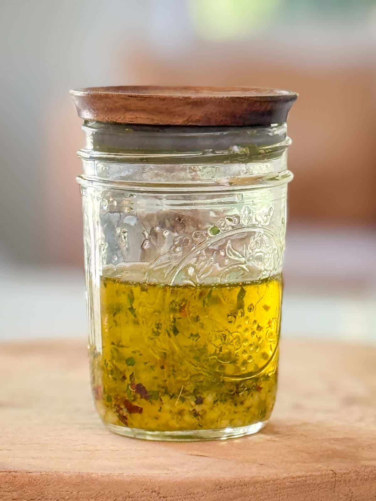 Golden garlic oil recipe in a small glass jar with crushed garlic and herbs on a rustic board.