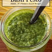 An open jar of homemade basil pesto with a spoon to show flecked texture.