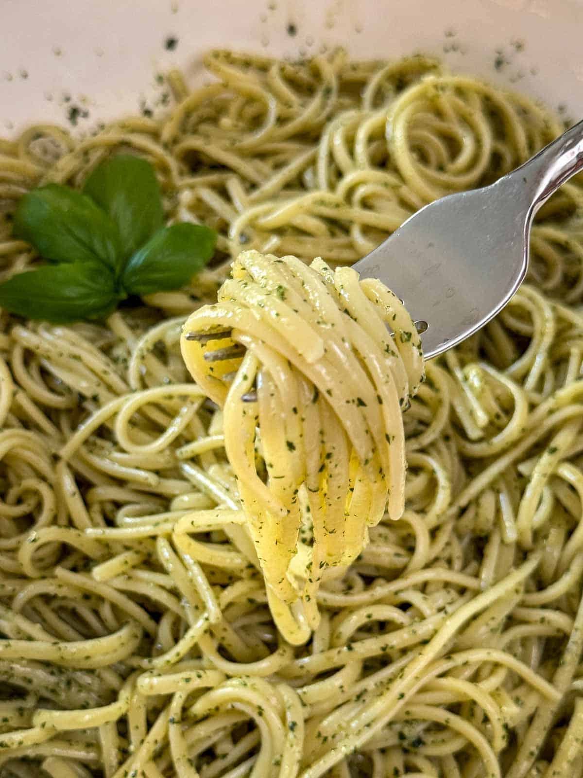 Easy pesto pasta twirled on a fork with Parmesan and basil garnish.