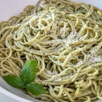 Basil pesto pasta recipe served in a white bowl, coated in fresh basil pesto sauce and topped with Parmesan cheese.