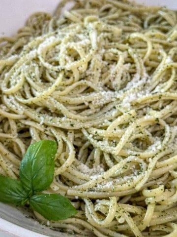 Basil pesto pasta recipe served in a white bowl, coated in fresh basil pesto sauce and topped with Parmesan cheese.
