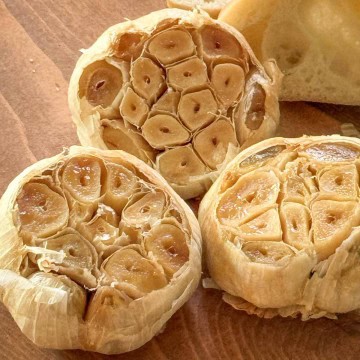 Rustic hero shot of roasted garlic with bread, salt, and olive oil on wooden board.