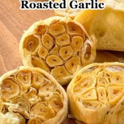 Rustic hero shot of roasted garlic with bread, salt, and olive oil on wooden board.