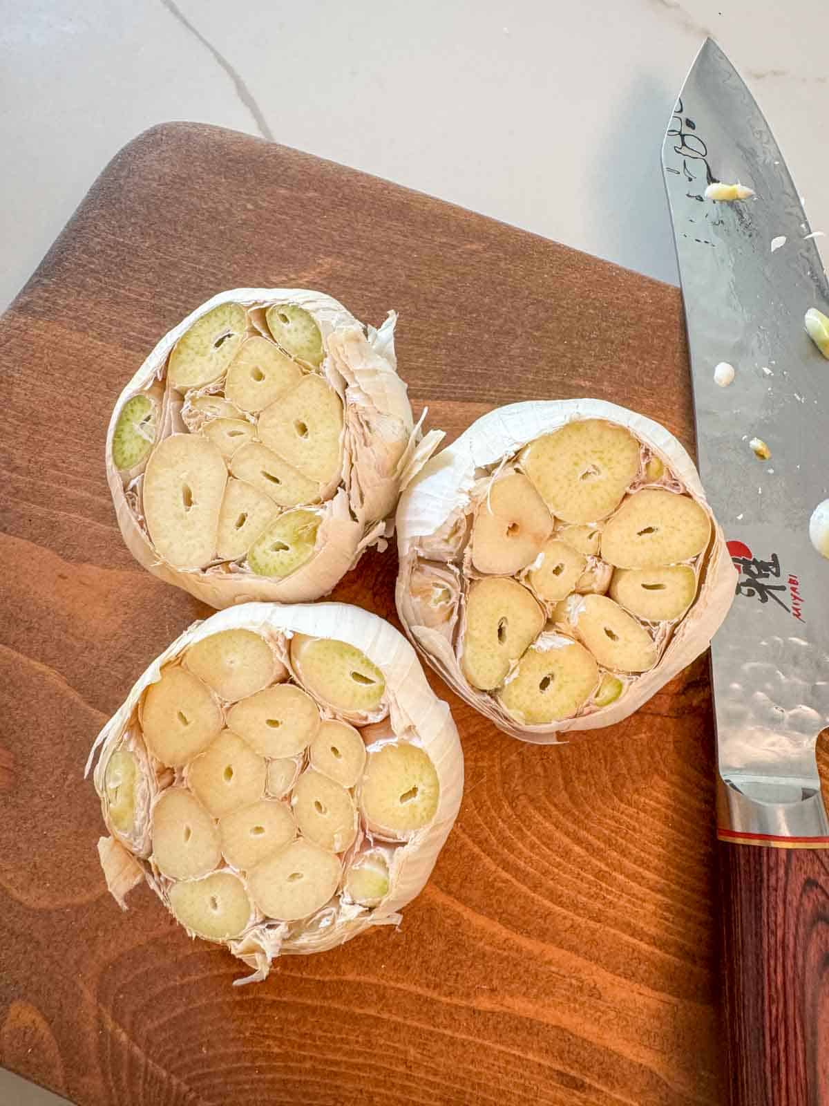 Whole garlic head on cutting board with top sliced off, cloves exposed, ready for roasting.