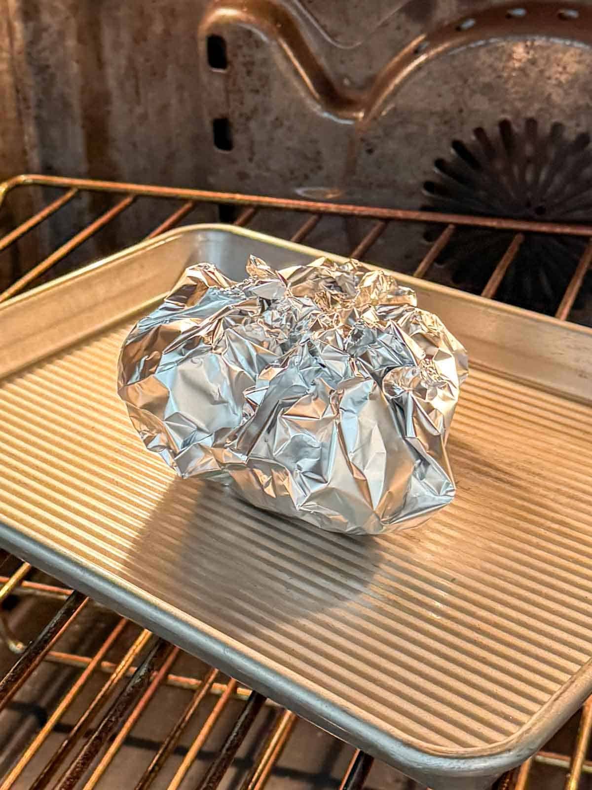 Foil-wrapped garlic head on baking sheet about to be roasted.
