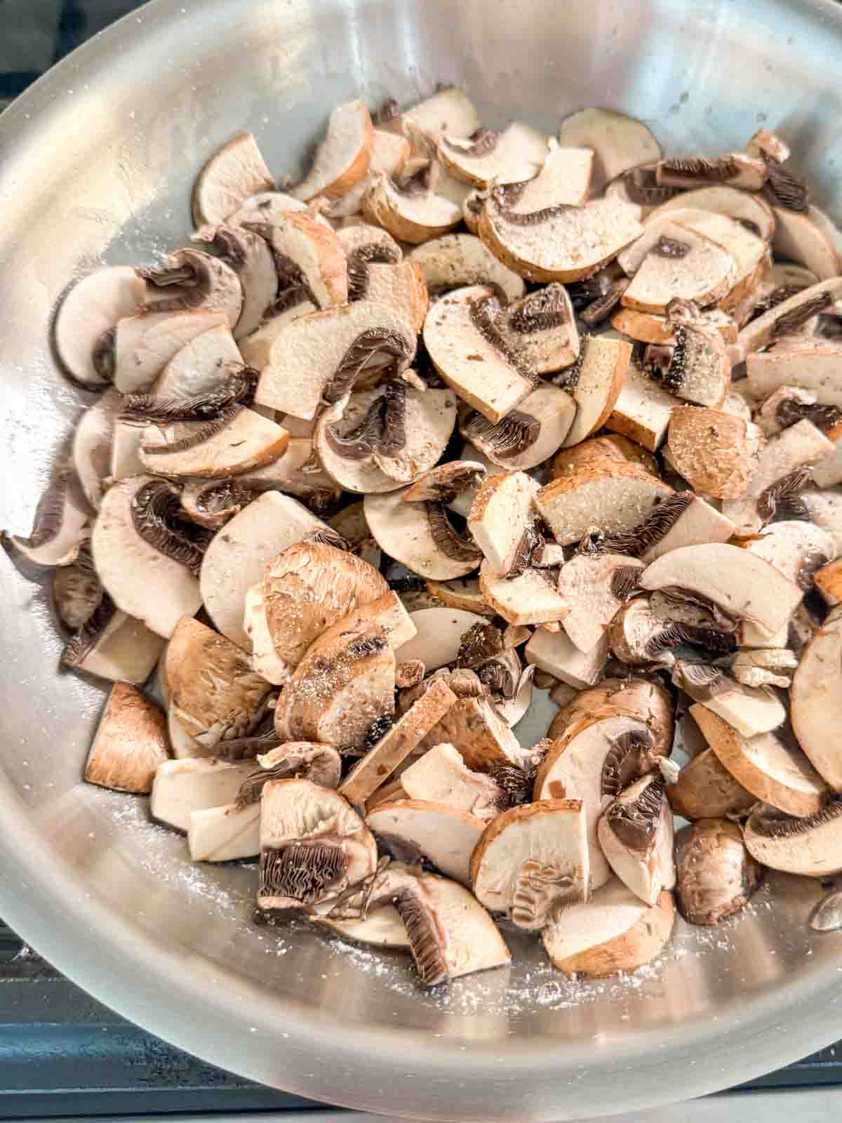 Thinly sliced Crimini mushrooms in a skillet.