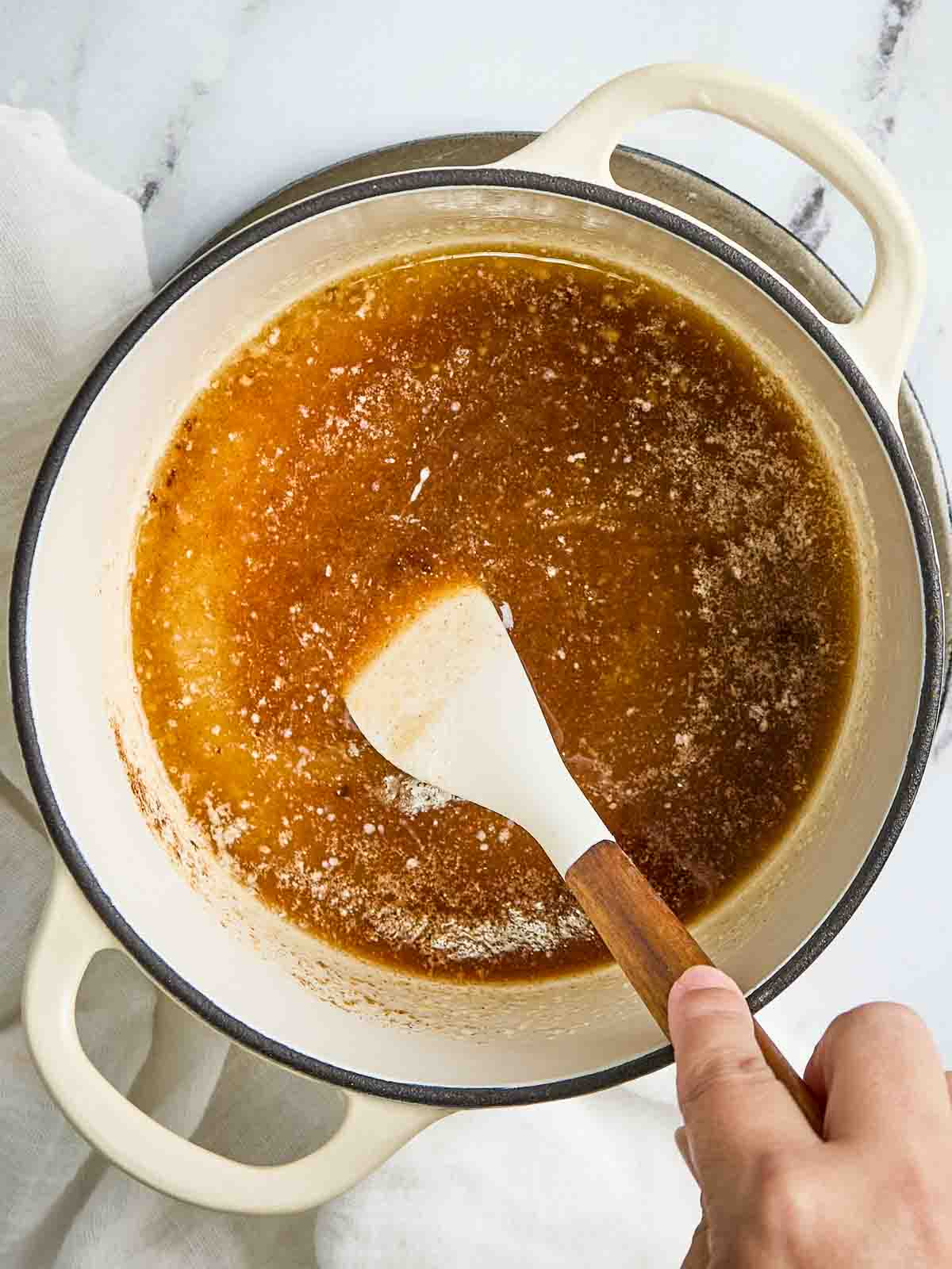 Caramel glaze for crescent roll apple dumplings recipe simmering in a small saucepan with a spoon stirring.