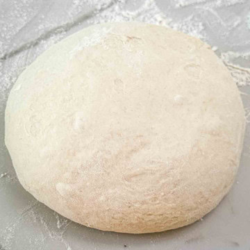 A round homemade pizza dough ball on a white background.