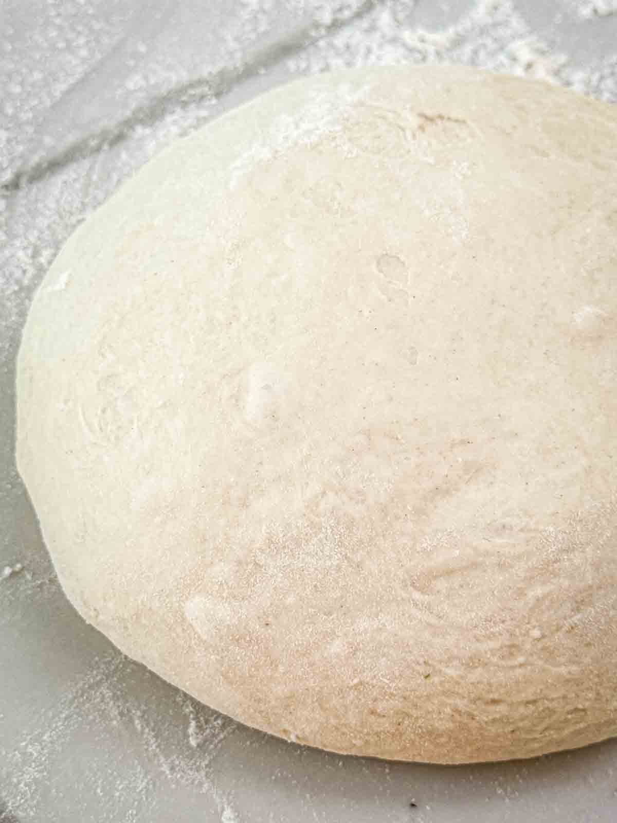 A round homemade pizza dough ball on a white background.