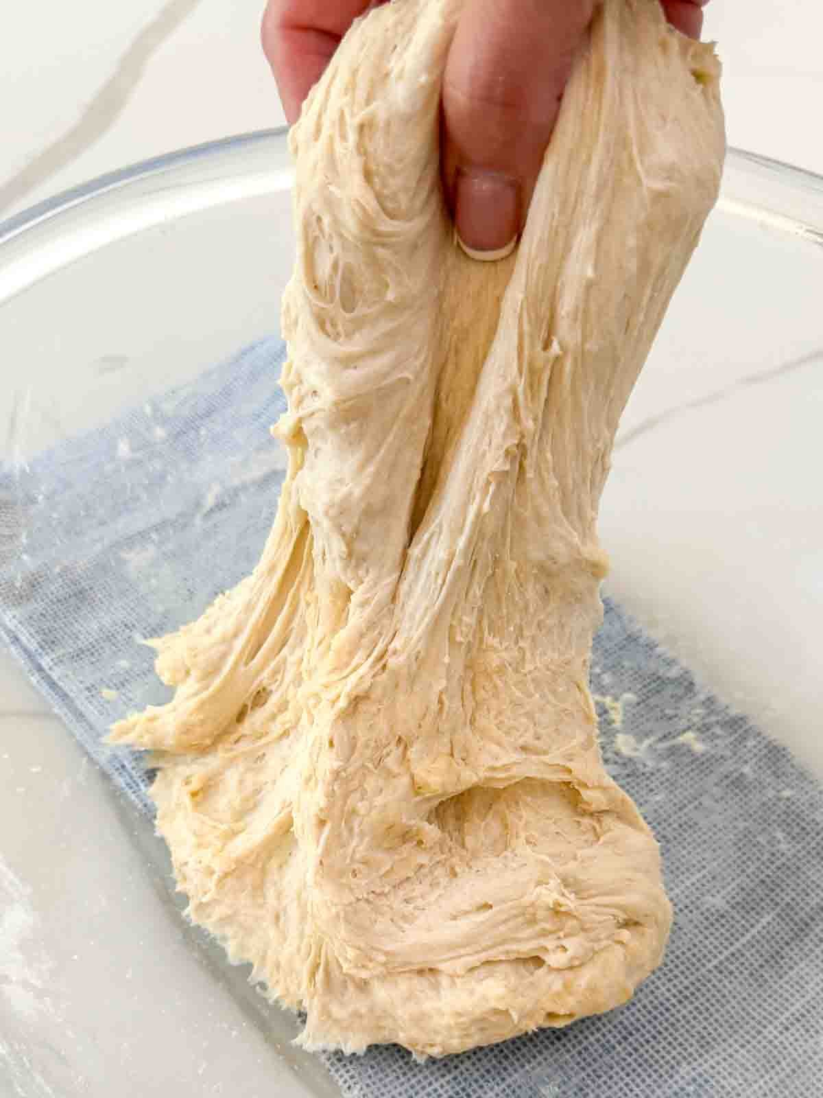 Hands stretching elastic pizza dough on a floured surface.