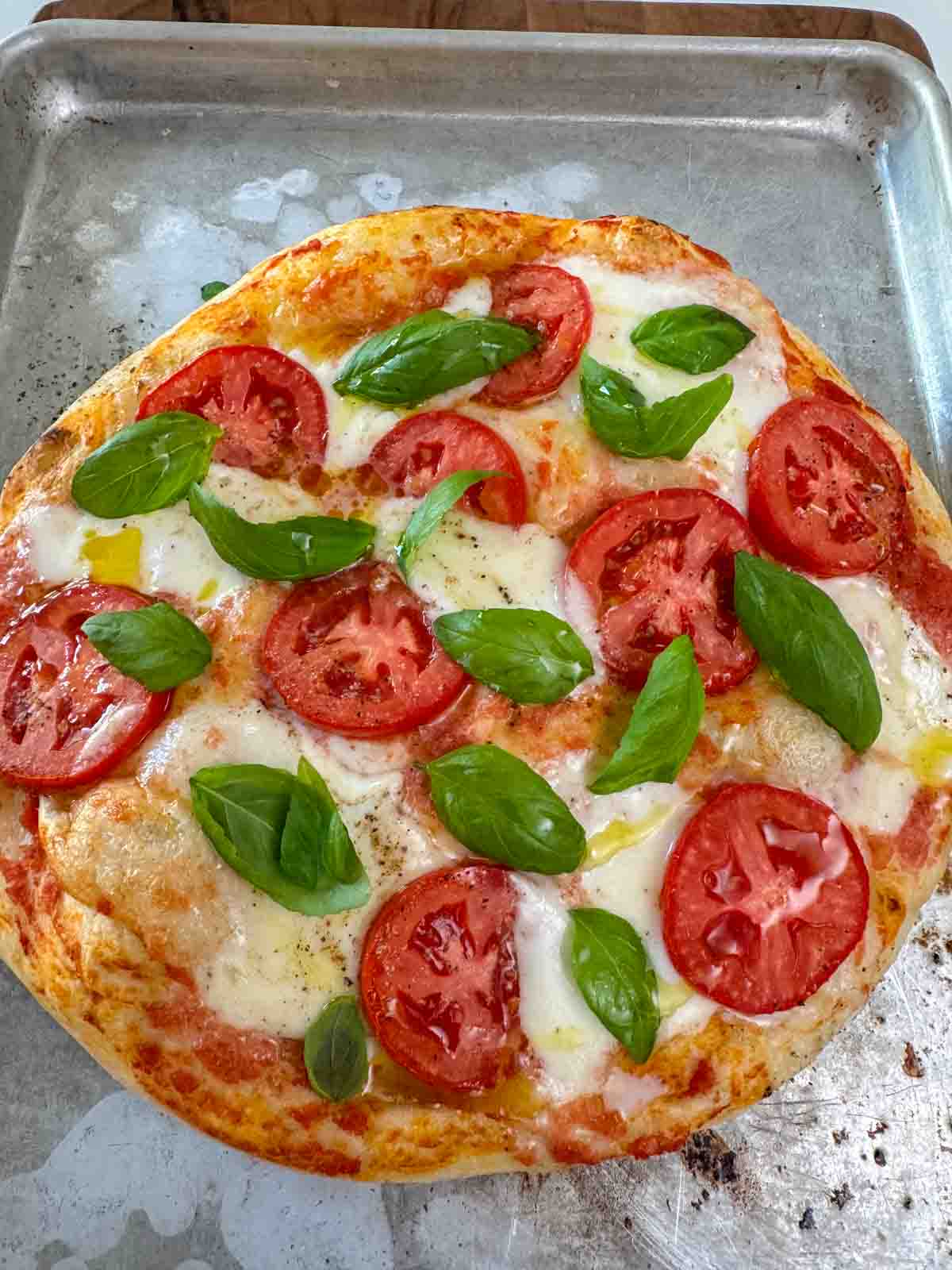 Freshly baked Margherita pizza on a wooden board, topped with melted mozzarella and fresh basil.