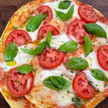 Freshly baked Margherita pizza on a wooden board, topped with melted mozzarella and fresh basil.