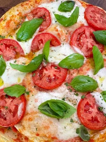 Freshly baked Margherita pizza on a wooden board, topped with melted mozzarella and fresh basil.