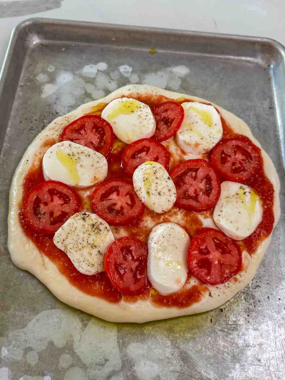 Mozzarella slices and tomato sauce on raw pizza dough, ready to bake.