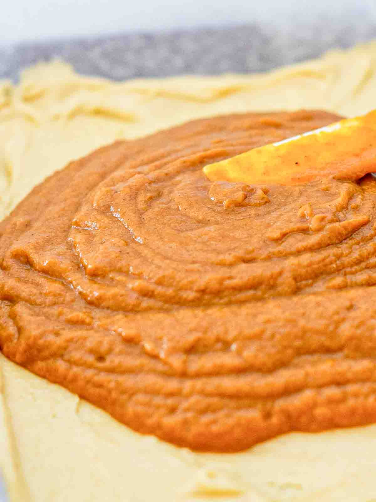Smooth, spiced pumpkin butter filling spread evenly over the crust layer in a 9x13 pan - rich orange color and glossy texture before adding the topping.
